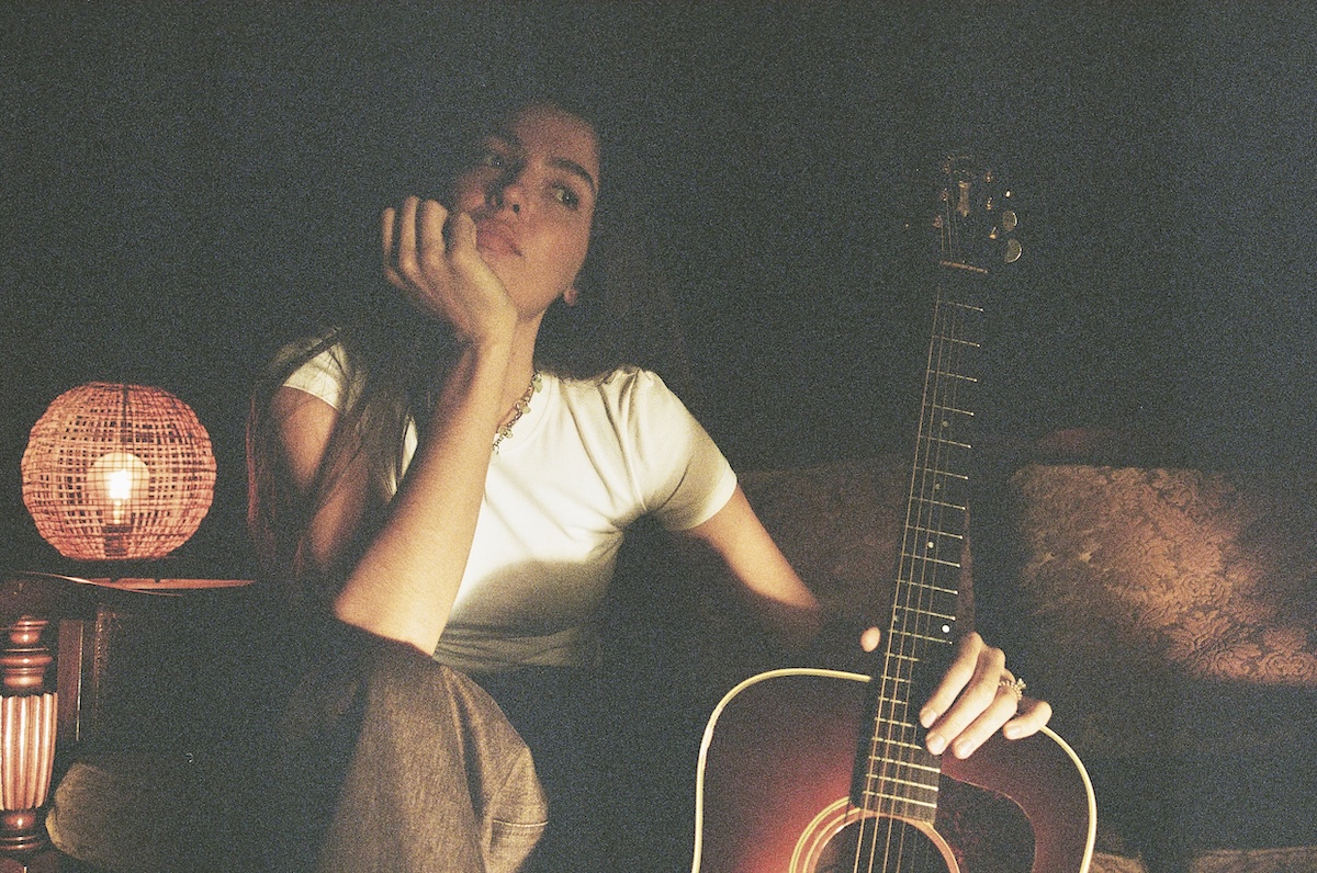 Portrait of singer-songwriter Kita Alexander resting her chin on her hand beside an acoustic guitar.